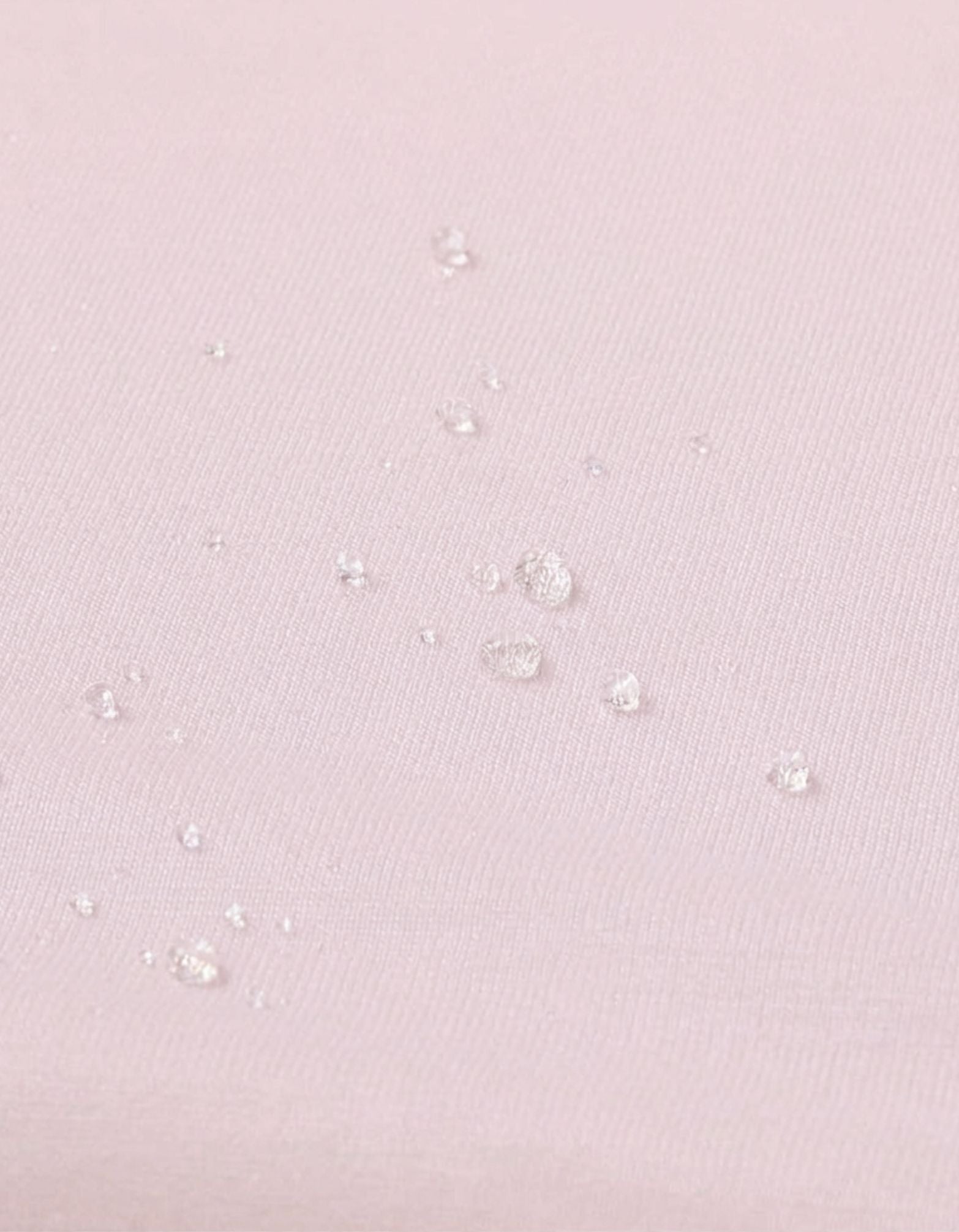 Detalle de la superficie impermeable de la sábana bajera con protector para minicuna 50x90 cm color rosa.