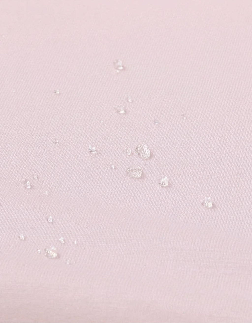 Detalle de la superficie impermeable de la sábana bajera con protector cuna 60x120 cm color rosa con gotas de agua.
