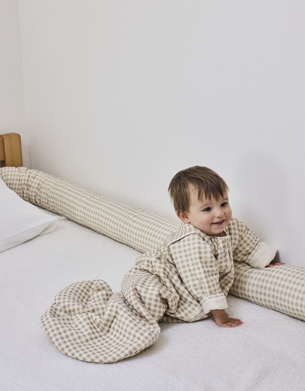 Cojín protector Vichy Sand colocado en la cama como barrera de seguridad para el bebé.