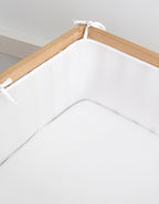 Detalle del protector de cuna Breath instalado en una cuna de madera, con tejido de malla 3D transpirable y cintas de sujeción ajustables.