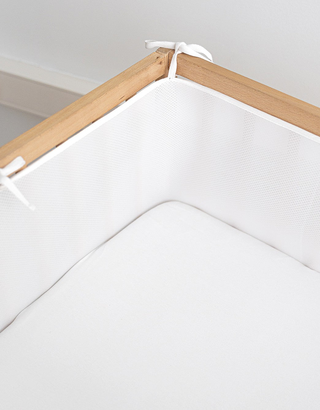 Detalle del protector de cuna Breath instalado en una cuna de madera, con tejido de malla 3D transpirable y cintas de sujeción ajustables.
