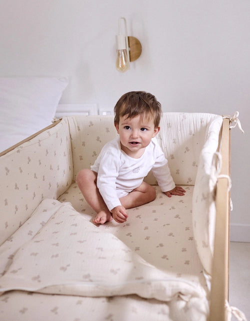 Protector de cuna Ducks estampado para bebé, acolchado y con lazos de sujeción, instalado en cuna de madera.