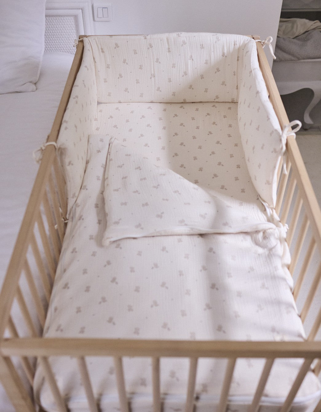 Protector de cuna Ducks estampado para bebé, acolchado y con lazos de sujeción, combinado con ropa de cama a juego en cuna de madera.