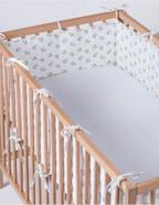 Protector de cuna Leaves de algodón orgánico con estampado de hojas, instalado en cuna de madera con laterales acolchados para proteger al bebé y aportar confort durante el descanso.