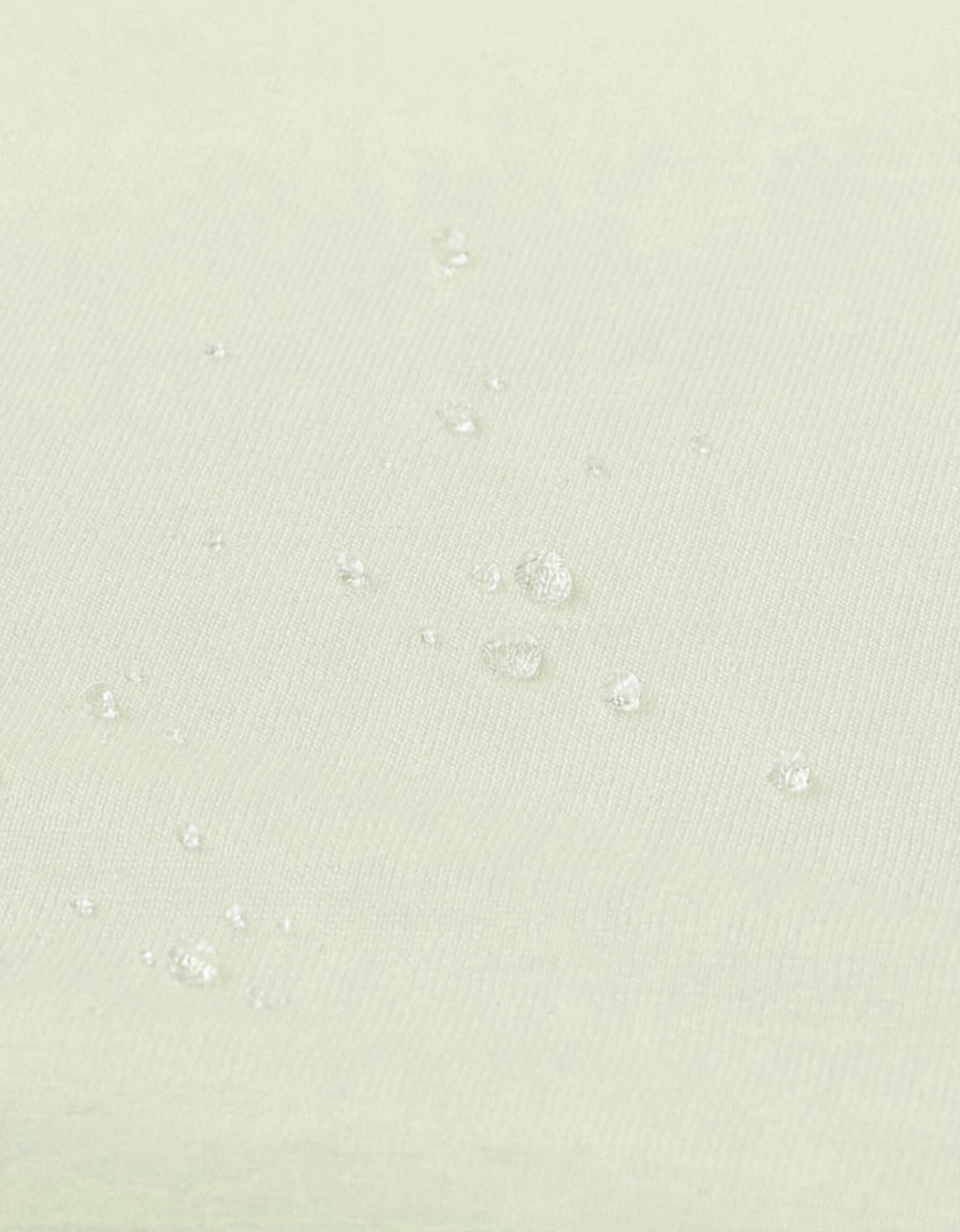 Detalle de la superficie impermeable de la sábana bajera con protector cuna 60x120 cm color arena con gotas de agua.