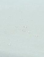 Detalle del tejido impermeable con gotas de agua en la sábana protectora para cuna color agua.