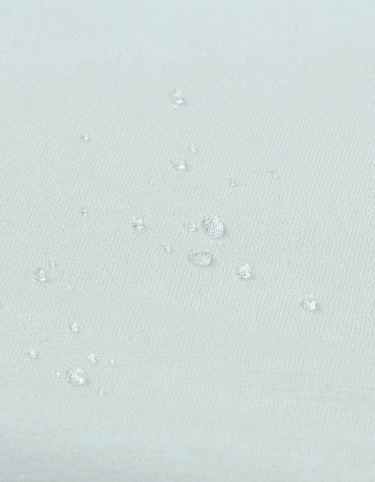 Detalle de la superficie impermeable de la sábana bajera con protector cuna 60x120 cm color agua con gotas de agua.