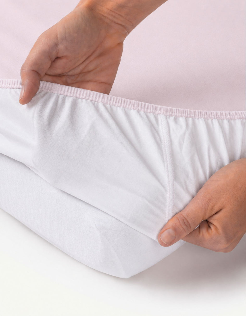 Detalle de la sábana bajera con protector impermeable cuna 60x120 cm color rosa ajustándose al colchón.