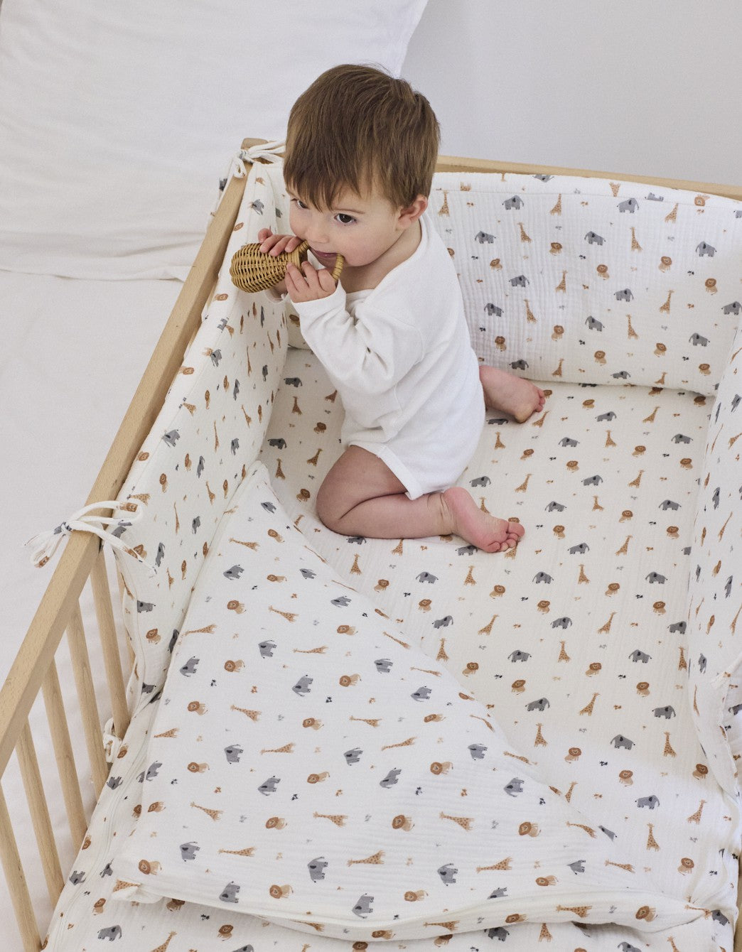 Bebé jugando sobre el saco de cuna Safari en una cuna de madera con estampado de animales.