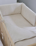 Saco de cuna Vichy Sand colocado en una cuna de madera, con estampado de cuadros vichy beige y protectores acolchados a juego alrededor del interior.