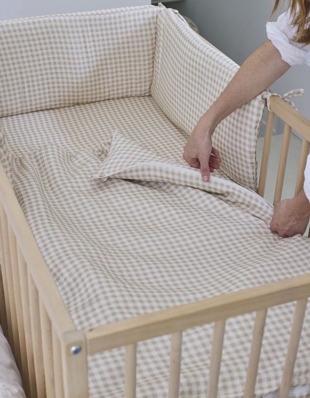 Persona colocando el saco de cuna Vichy Sand en una cuna de madera con estampado de cuadros vichy beige.
